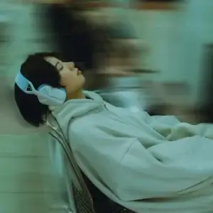 A woman wearing a hoodie and headphones sitting relaxed on a chair, suggesting a serene moment.
