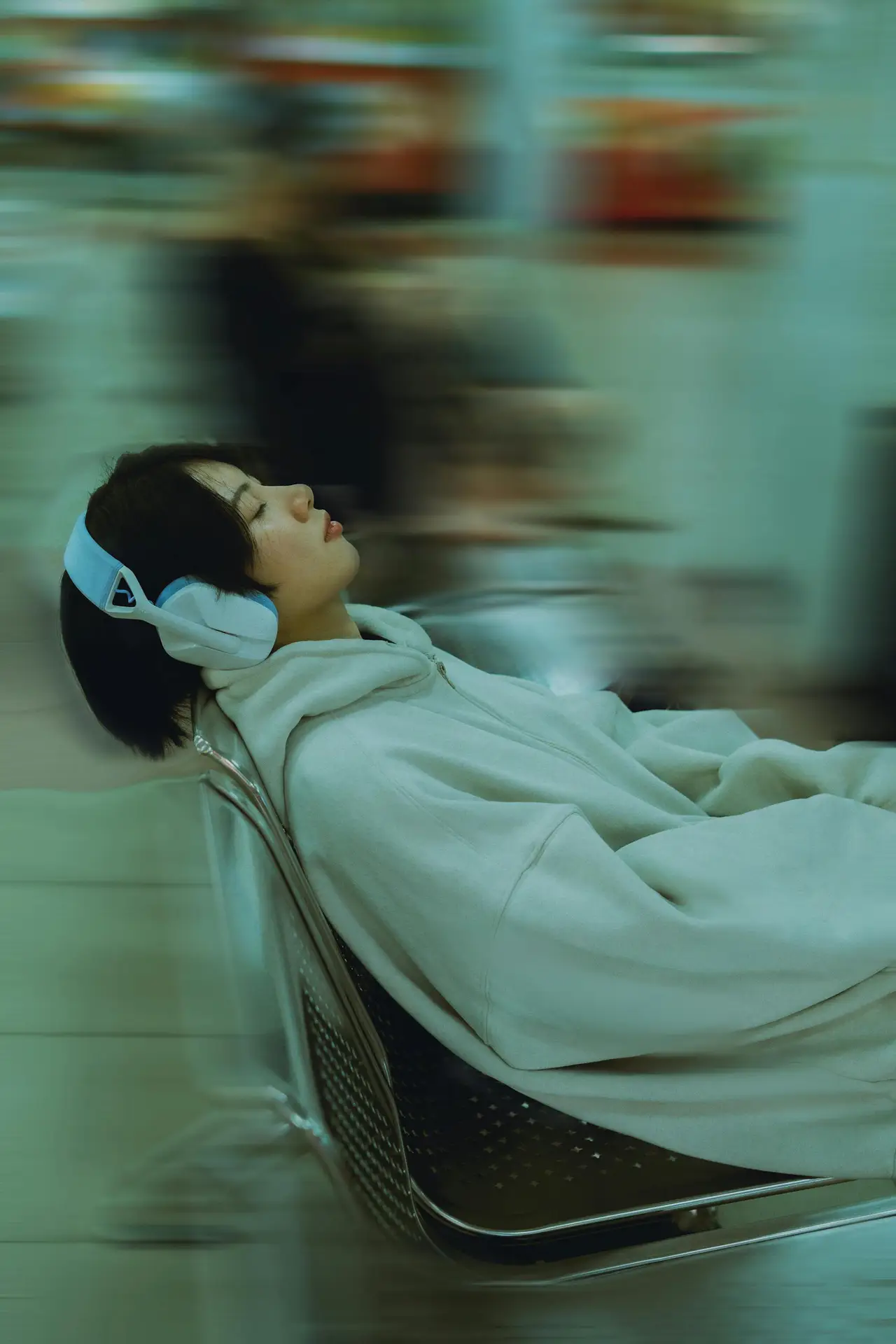 A woman wearing a hoodie and headphones sitting relaxed on a chair, suggesting a serene moment.