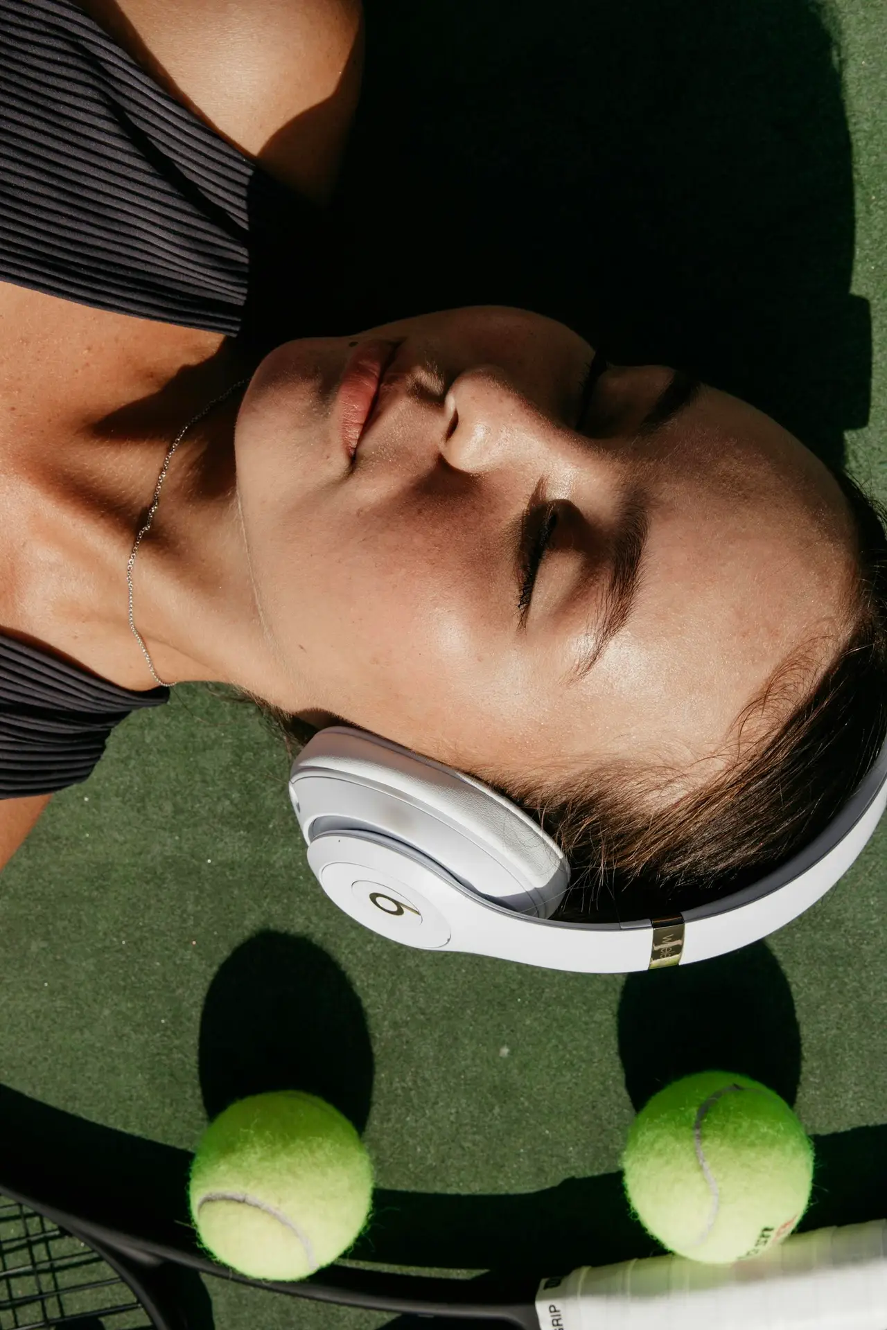 Relaxed woman on a tennis court with headphones and tennis equipment.
